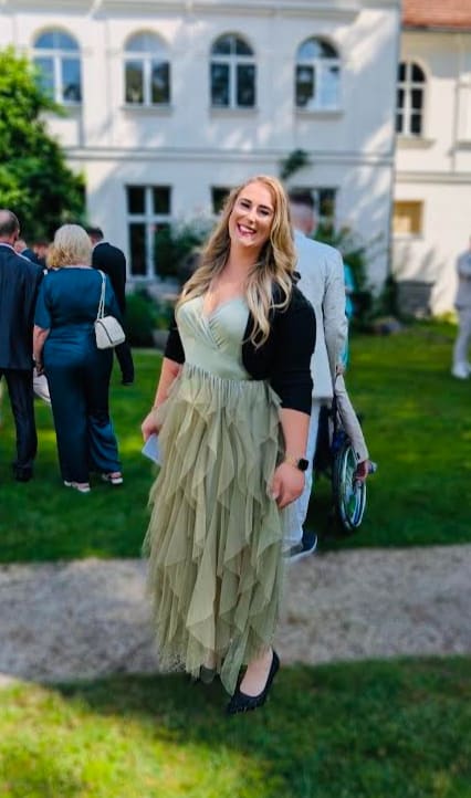 Pauline Hartmann lächelt in die Kamera, sommerlich gekleidet vor einem hellen Herrenhaus.
